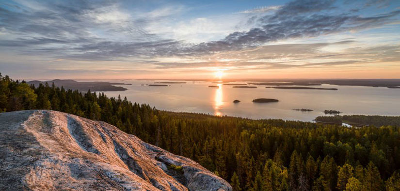 Vaaran laelta avautuva järvimaisema. Aurinko on juuri noussut horisontin takaa.