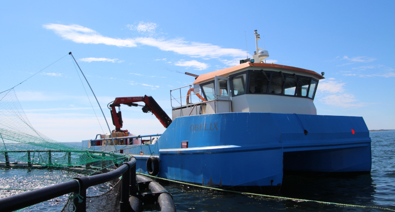 A utility vessel moored beside a cage on an offshore fish farm.