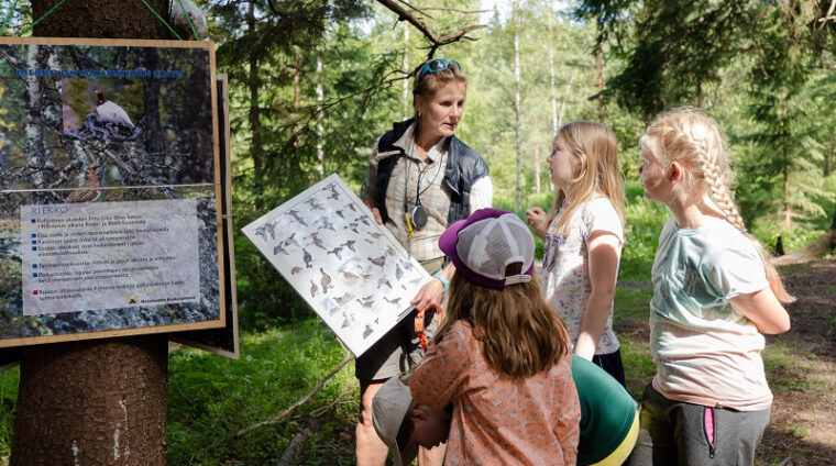 Lapset katsovat lajintunnistustaulua eräkummin ohjauksessa.