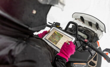 Woman looking at GPS device while sitting on a snowmobile.