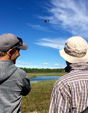 Kaksi miestä katsoo, kun drone lentää suon yläpuolella.