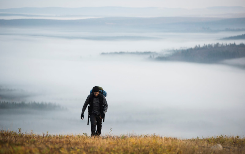 A man is climbing a slope with a misty hill landscape in the background.