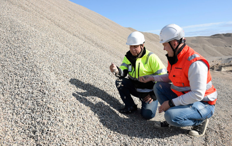 Two men dressed in work clothes look at the gravel on a gravel pit.