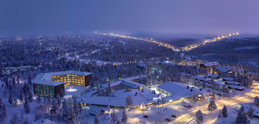 An aerial photograph of Lake Saariselkä, with an illustration of a big hotel. Ski slopes can be seen in the background. 