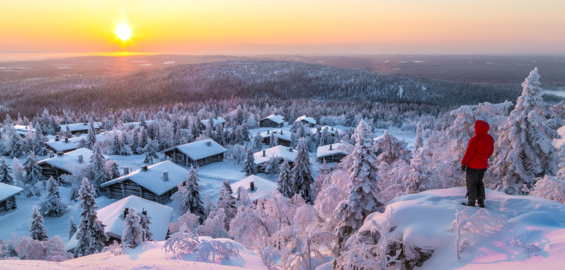 Mannen tittar på en stugby och en solnedgång från en snöig klippa