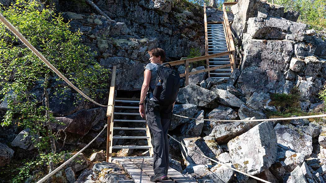 Retkeilijä seisoo kallioisessa laaksossa, edessä ylös rinteeseen nousevat portaat.