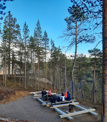 Ihmiset istuvat tunturin rinteellä taukopaikan lankkupenkeillä vastatusten.