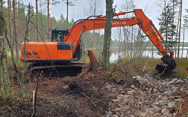 Kaivinkone tekee kivien muodostamaa kynnystä ojan suulle lammen rantaan.