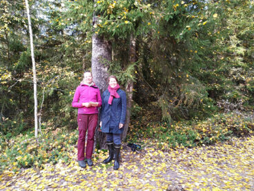 Kaksi Metsähallituksen hanketyöskentelijää vierekkäin puunrungon edessä.
