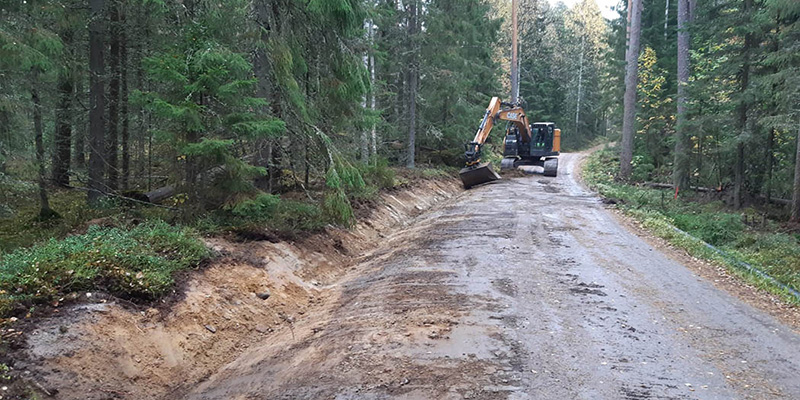 Kaivuri kaivaa hiekkatien reunaan ojaa metsän keskellä.