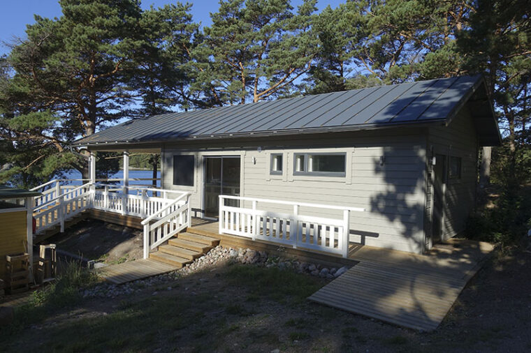 Grey, one-storey wooden building with stair and ramp access. The terrace has handrails around it.