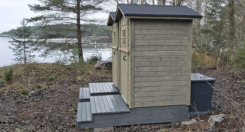 Två torrtoaletter i trä som är byggda intill varandra nära stranden.