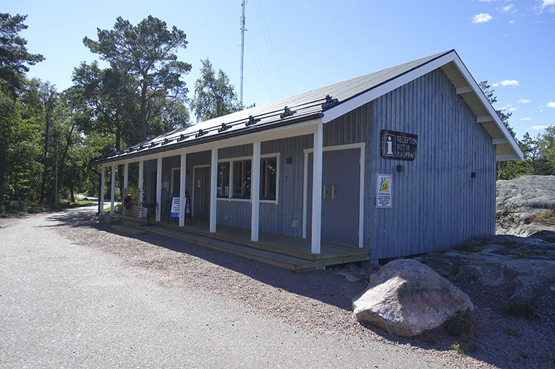 Grå träbyggnad i en våning. Framför byggnaden går en asfalterad väg.