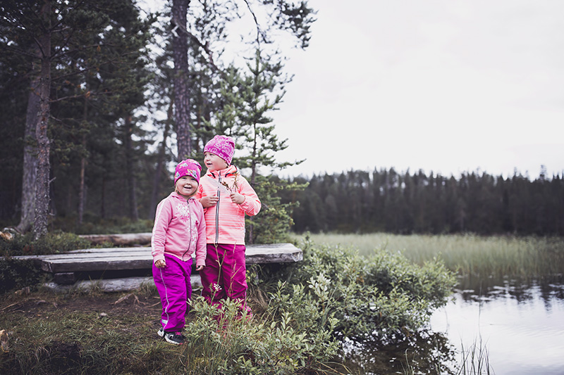 Två barn står vid dammen. Ett annat barn håller en vit fjäder.