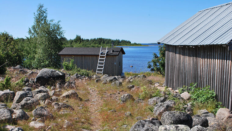 Meren rannalla kivikossa polku ja maalaamattomia, lautarakenteisia mökkejä.