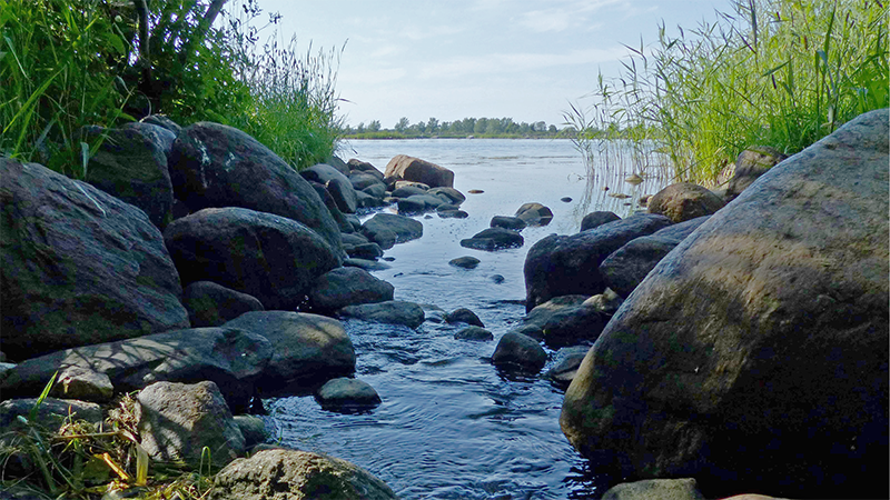 Puro virtaa kivien välissä merenlahteen. Taustalla matala saari.