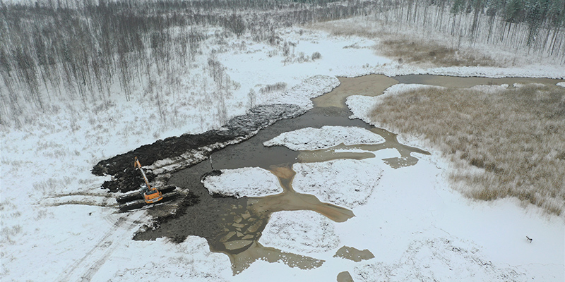 An excavator on the shore of a shallow lake in winter.