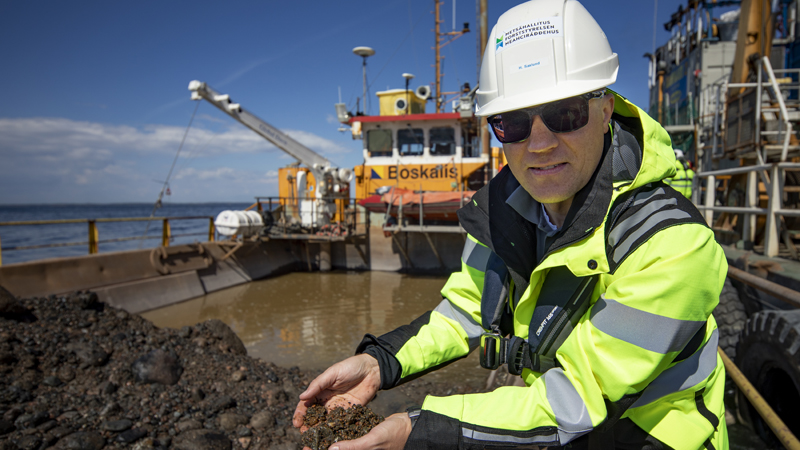 The man is squatting at the stone anemone lifted into the barge and shows it in his hand.