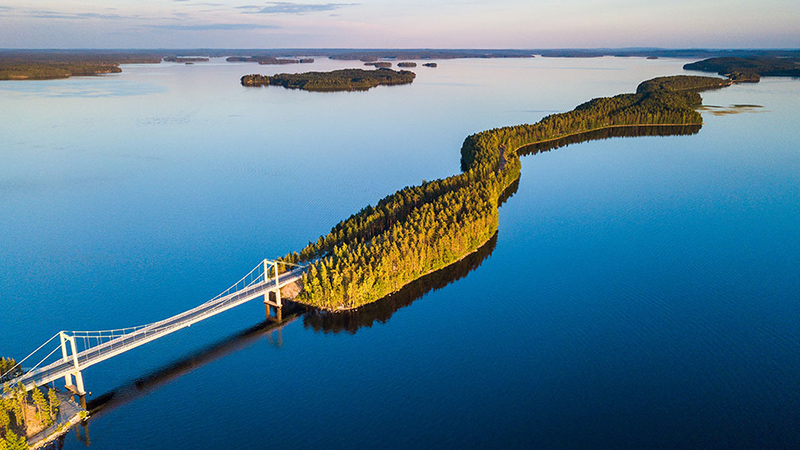 Ilmasta kuvattu tyyni järvimaisema kesällä, järven poikki kulkee kapea harju, jossa metsää ja siltoja.