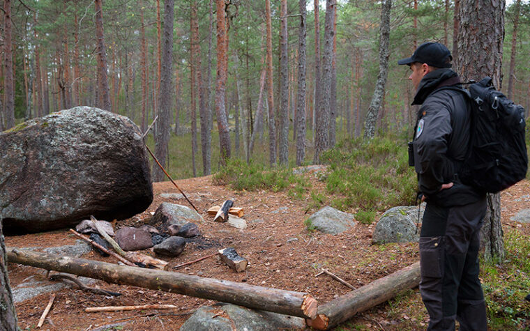 Metsässä suuren kiven vieressä poltettu nuotiota niin, että kivi on nokeentunut ja nuotion viereen katkaistu kokonainen puunrunko.