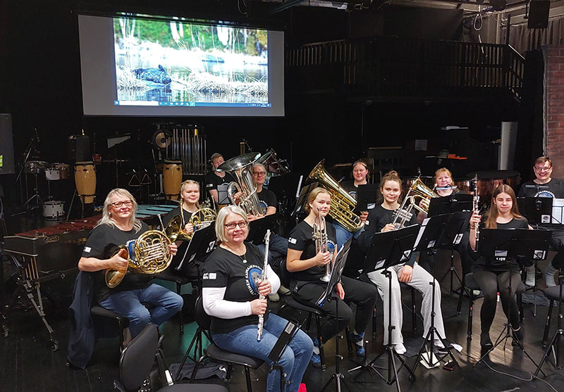 Musicians sitting and holding their music instruments, on the screen behind them a photo of saimaa ringed seal.