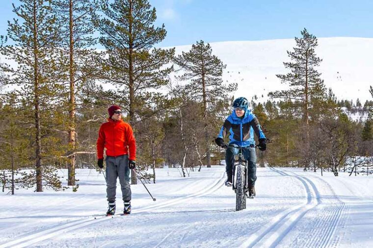 Pyöräilijä ja hiihtäjä rinnakkain aurinkoisena talvipäivänä.