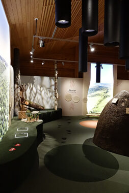 Näyttelyn huone, missä seinillä suuria maisemakuvia, seinustoilla kaarevia, matalia penkkejä.