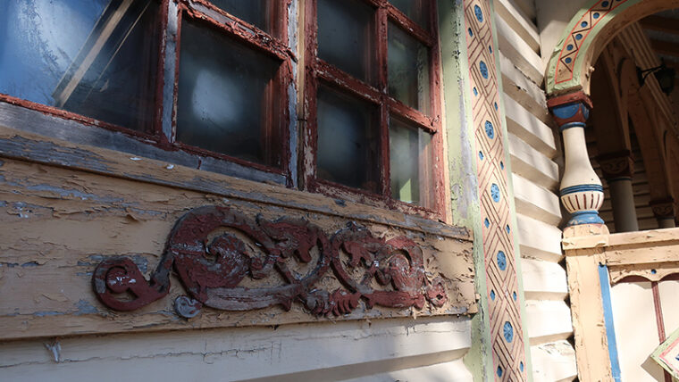 Puurakennuksen seinää, missä ikkunanpokia ja veistettyjä koristeosia, joista irtoaa maalia.