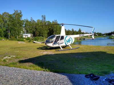 Valkoinen helikopteri nurmikentällä. Taustalla näkyy ranta ja metsikköä.