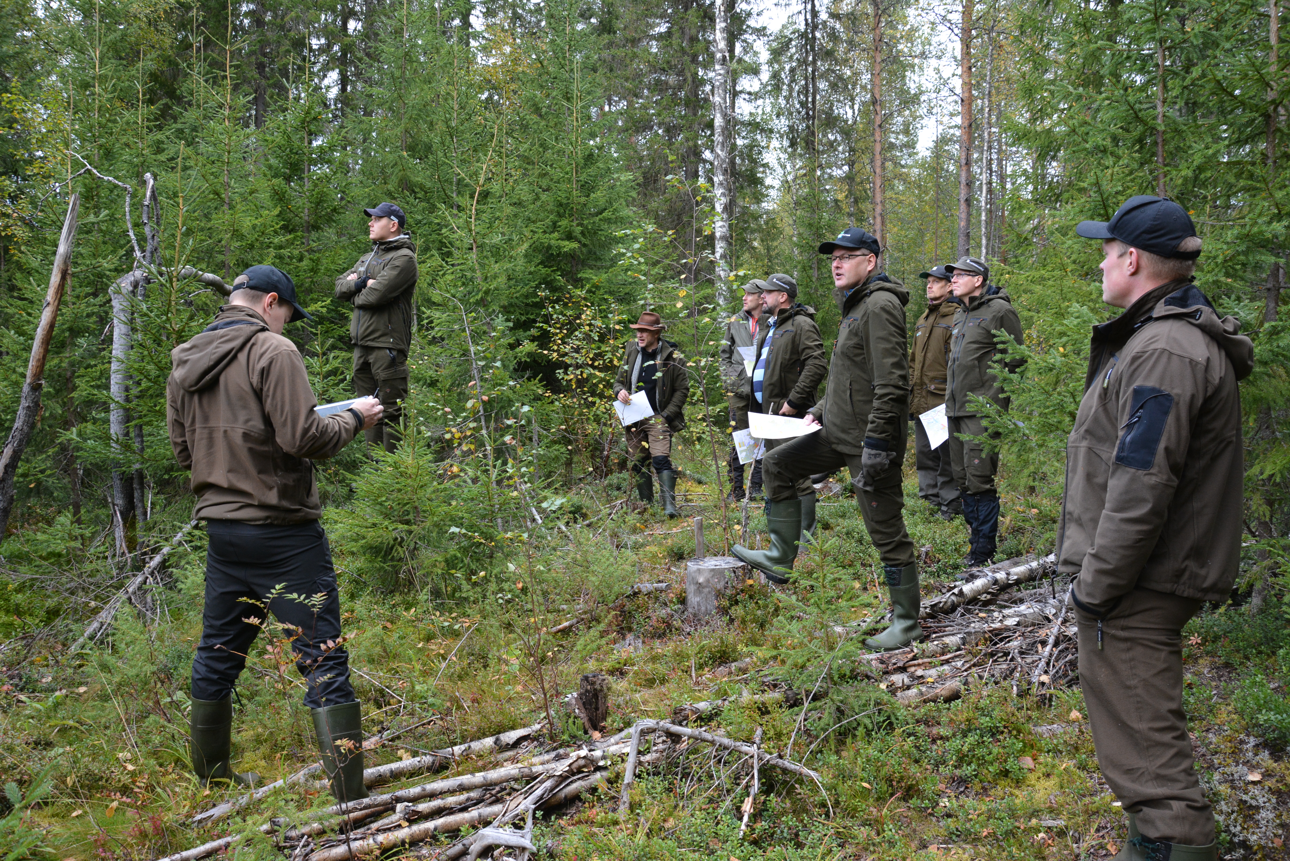 Noin kymmenen henkilöä alkusyksyllä metsässä katselemassa hakkuujälkeä.