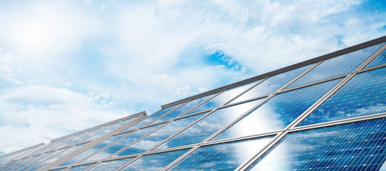 Aurinkopaneleeita valkoisten harsopilvien osin peitt&auml;m&auml;n sinisen taivaan alla.