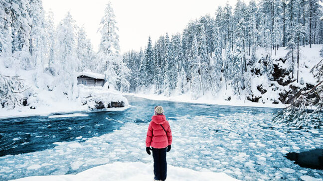 Nuori tyttö seisoo talvella osittain sulan joen äärellä.