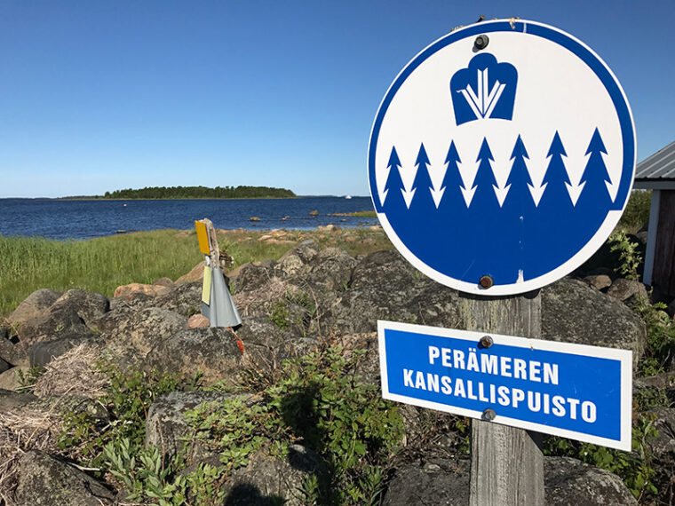 Kansallispuiston kyltti, taustalla on rantaa ja merta.