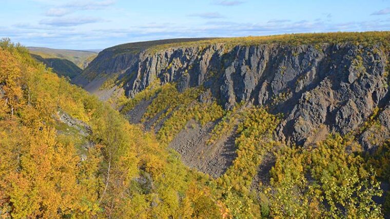 Etualalla v&auml;rikk&auml;iden puiden peitt&auml;m&auml; rinne, jonka takan rotkolaakso ja sen kallioinen vastareuna.