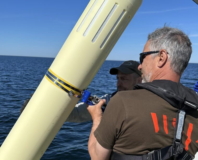 Kaksi miest&auml; seisoo veneess&auml;. He ovat nostaneet veneen laitaan vasten poijun, jossa on lepakkodetektori