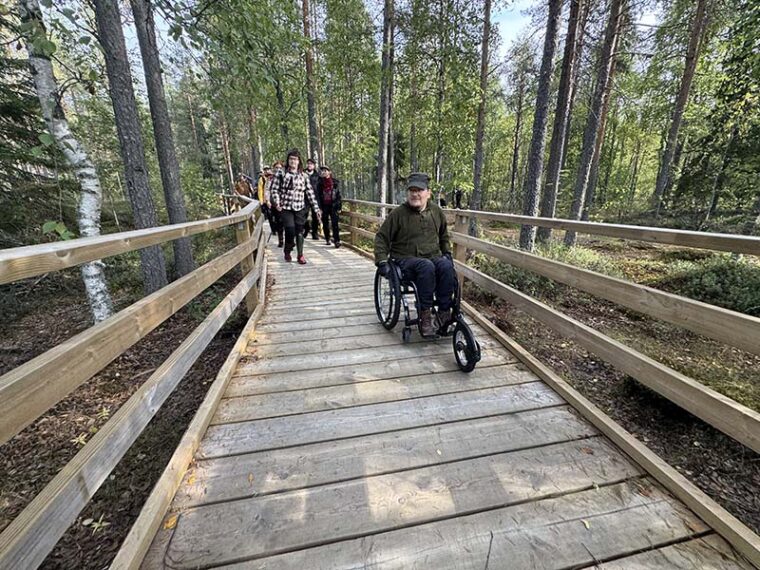 Ryhmä retkeilijöitä leveällä lankkupolulla. Ensimmäinen kulkee pyörätuolilla.
