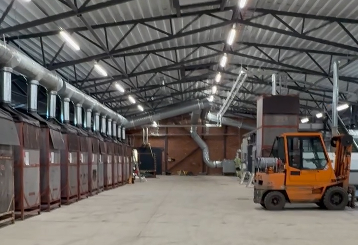 Iso teollisuushalli, jonka vasemmassa laidassa on 12 pystymallista säiliötä, joiden päällä on huppu ja ilman poistoputki. Oikeassa laidassa on etualalla trukki.