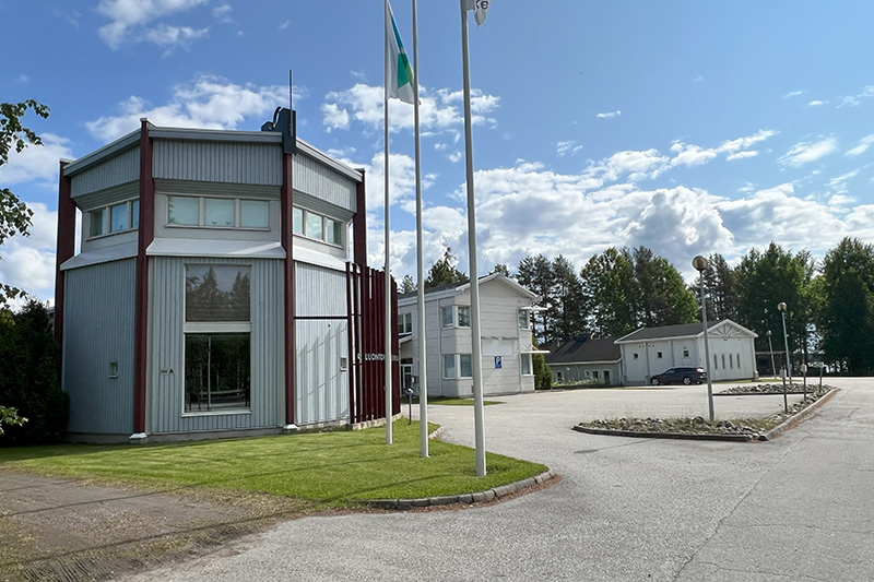 Kolme vaaleaa puurakennusta ja laaja pysäköintialue.
