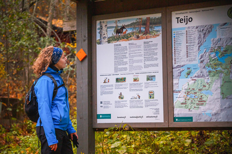 Retkeilij&auml; seisoo syksyll&auml; ison infotaulun luona ja lukee sit&auml;.