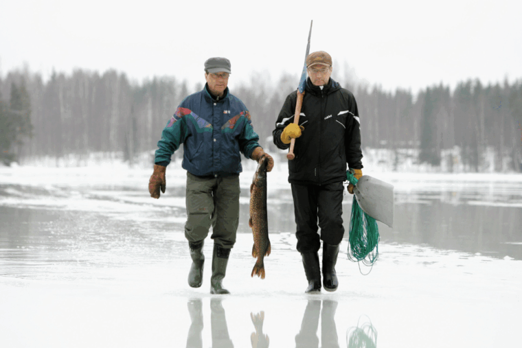 Kaksi miestä kävelee jäällä ja toisella on iso hauki kädessään.