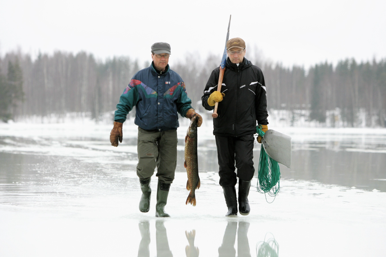 Kaksi miestä kävelee jäällä ja toisella on iso hauki kädessään.