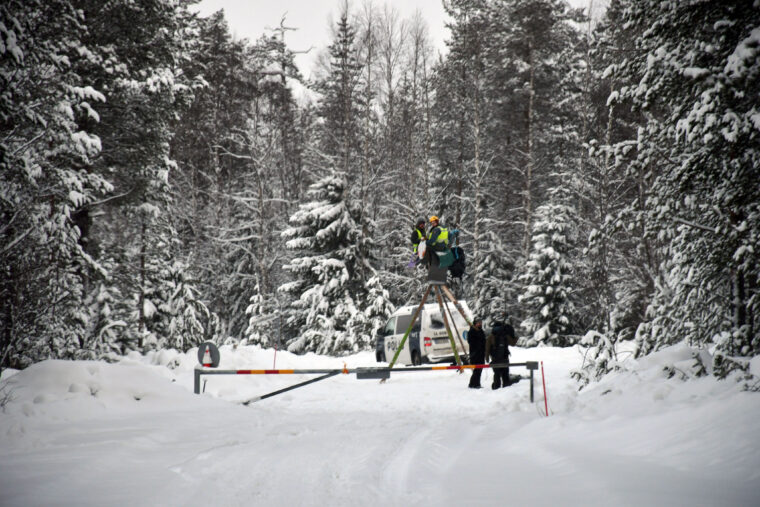 Henkil&ouml;it&auml; ja poliiseja tiell&auml; lumisessa mets&auml;ss&auml;.
