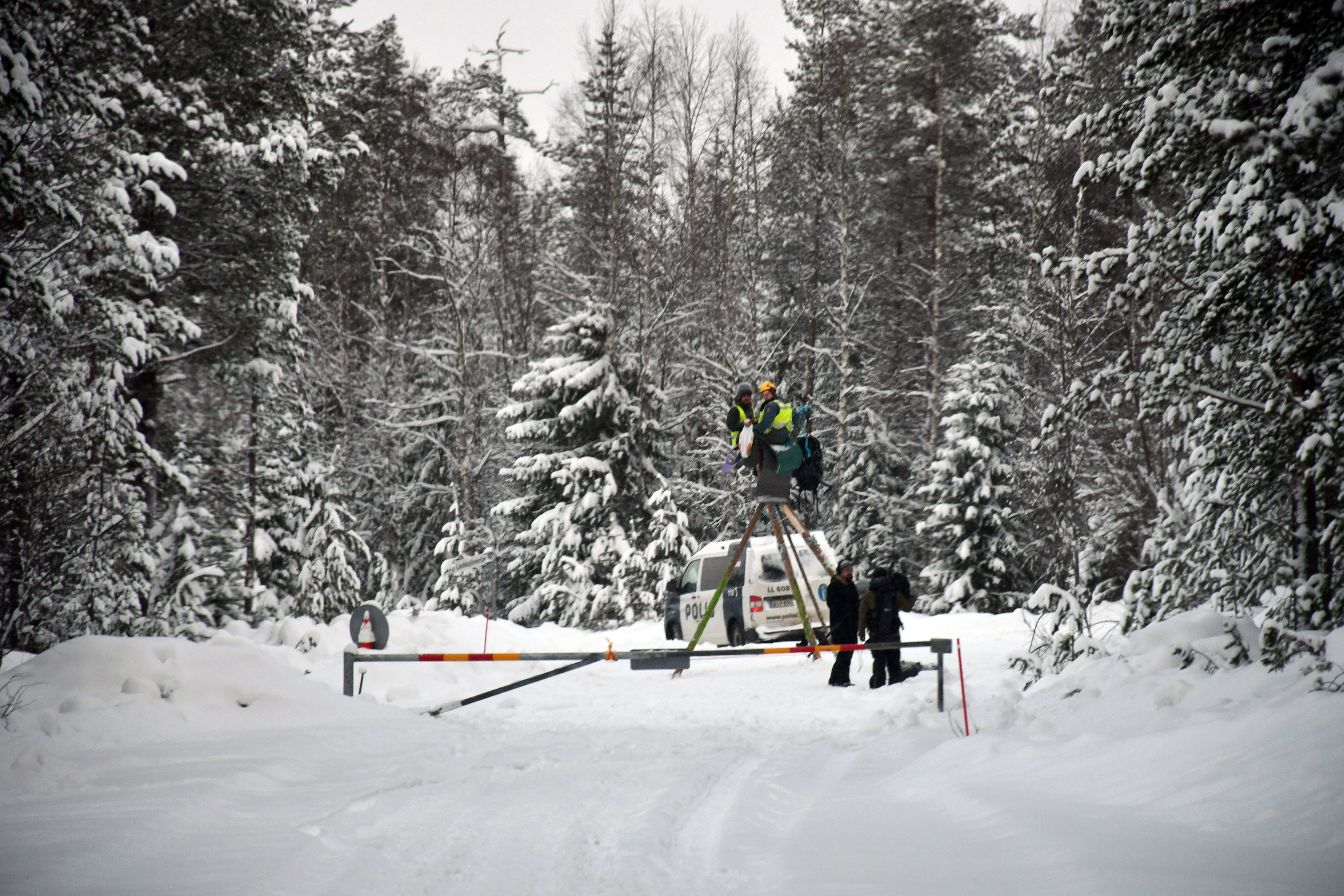 Henkil&ouml;it&auml; ja poliiseja tiell&auml; lumisessa mets&auml;ss&auml;.