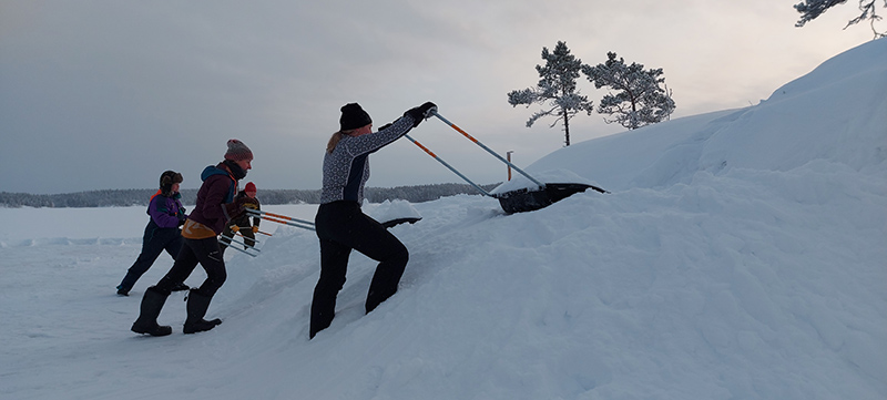 Ihmiset kolaavat lunta jäällä kinoksiksi.