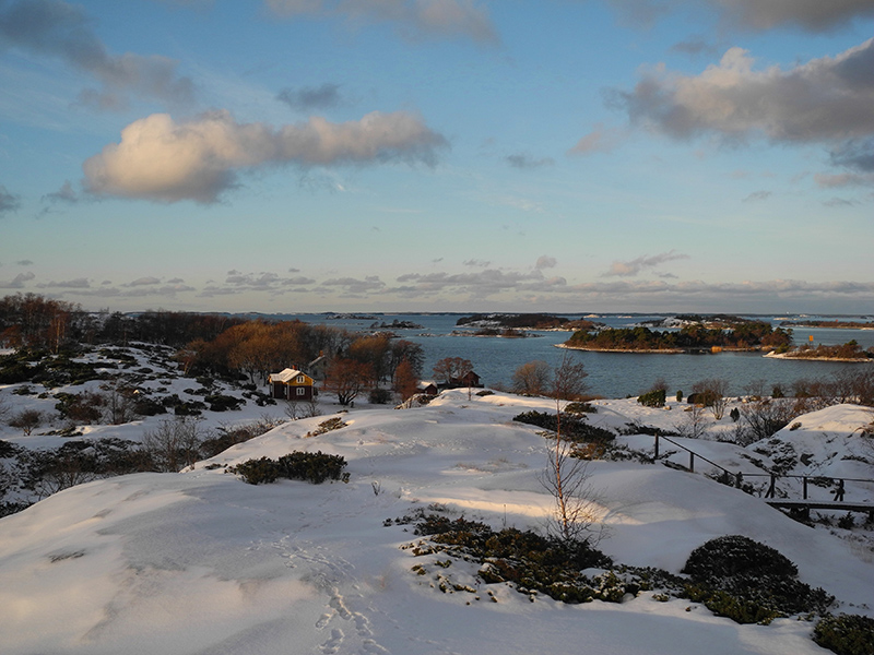 Vinterlandskap i skärgården. Strandklippan är täckt av snö. Havet i bakgrunden är isfritt.