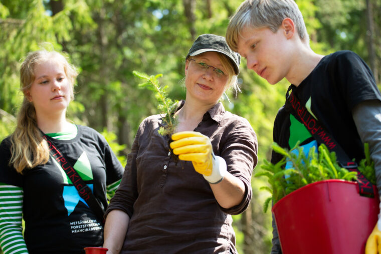 Esihenkilö esittelee kahdelle istuttajalle puuntaimea.