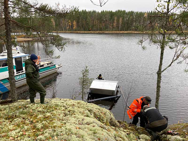 Neljä henkilöä asentamassa keinopesää saaren rantaan.