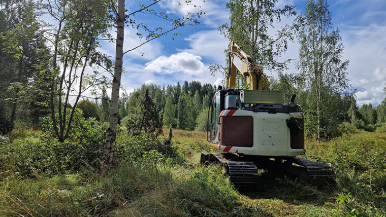 Kaivinkone metsän reunassa raivaamassa.