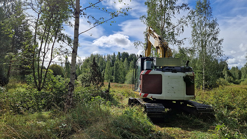 Kaivinkone metsän reunassa raivaamassa.
