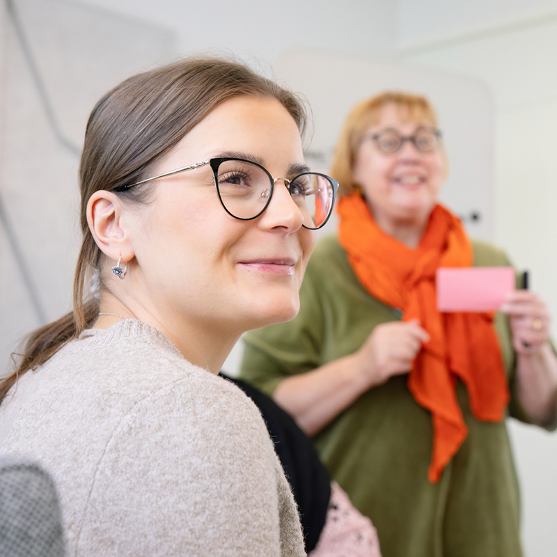 Kaksi hymyilevää naista, toisella on post-it-lappu kädessä.